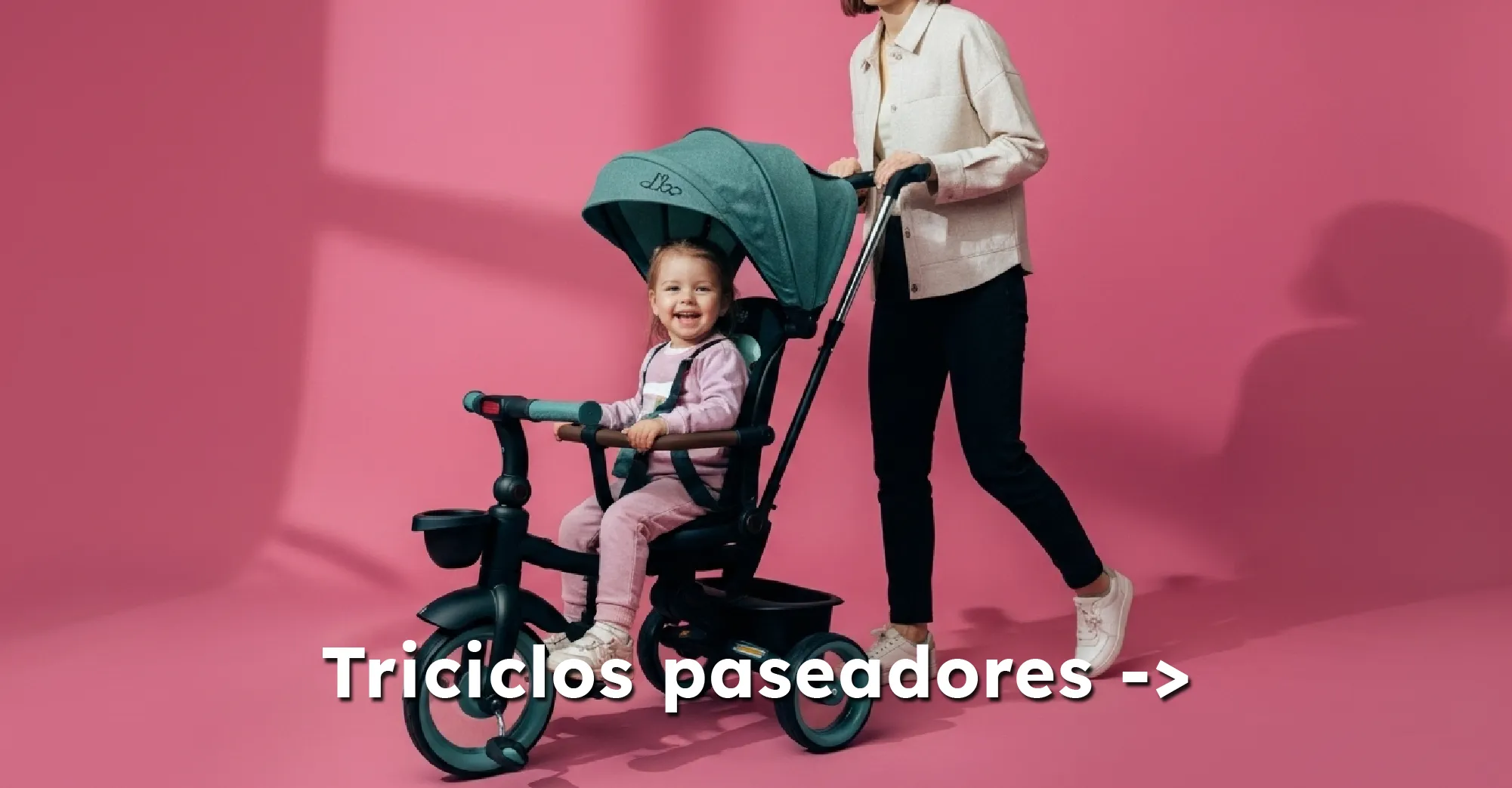 Bebé sonriendo en triciclo paseador verde con mango de empuje, acompañado por su madre